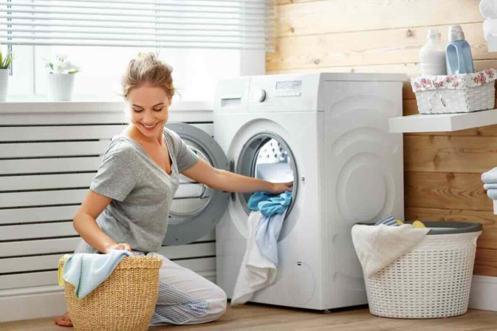 Donna felice prende vestiti da cestino di vimini e li inserisce nella lavatrice