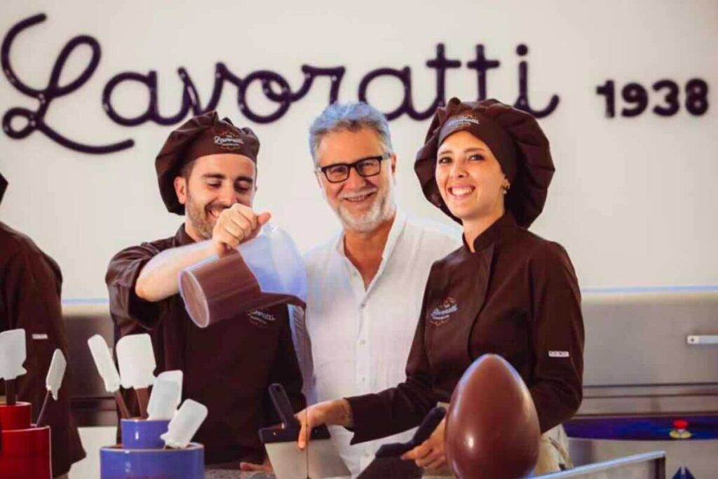 Fabio Fazio e due cioccolatieri, un uomo e una donna, uovo di Pasqua sul tavolo e sul retro scritta "Lavoratti"